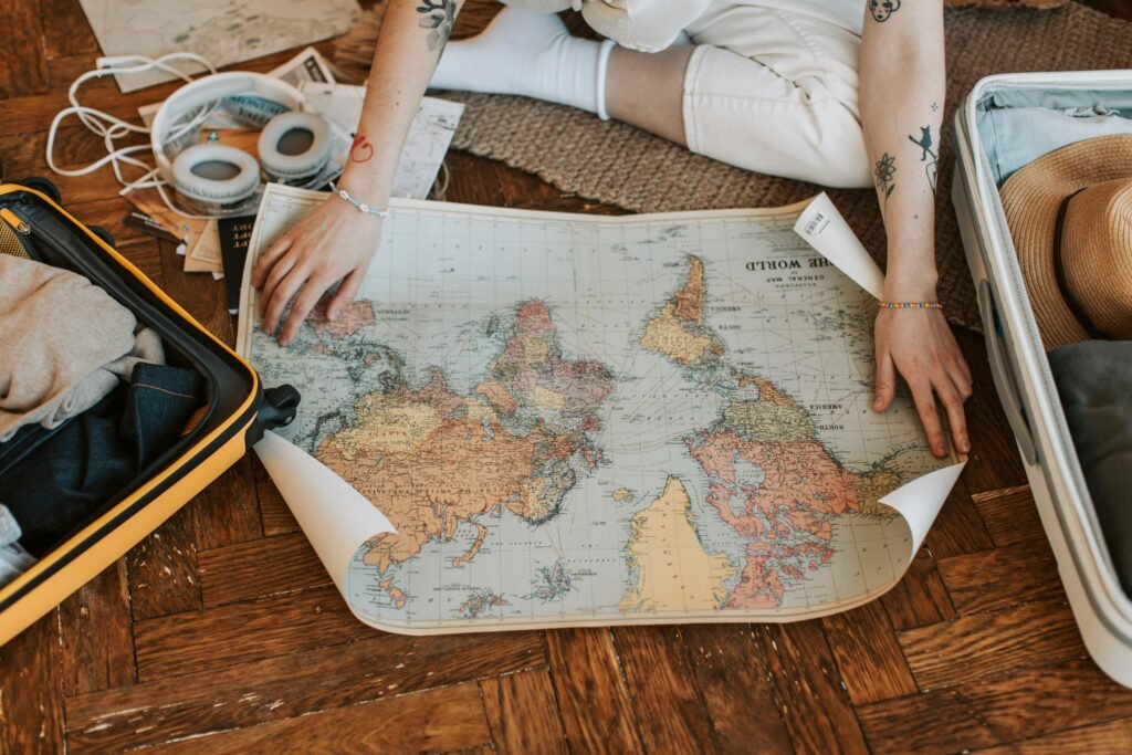 A traveler plans a journey, sitting on the floor with a world map and suitcase filled with essentials.